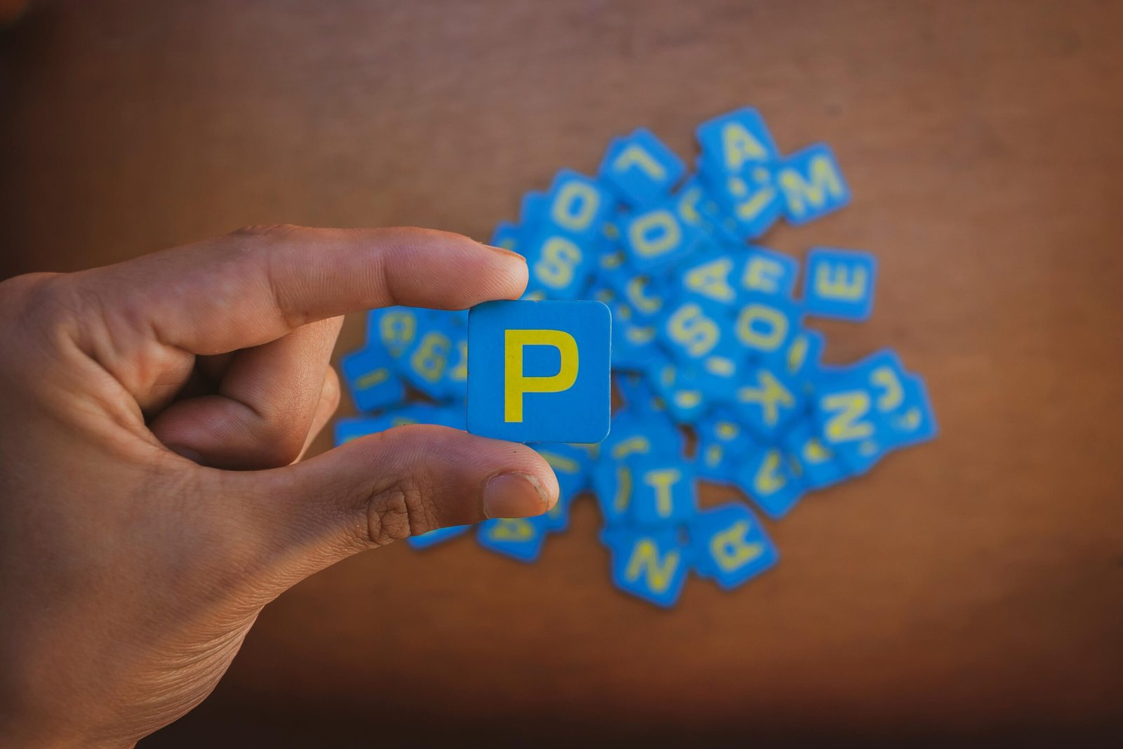 Close-up of a hand picking a blue letter tile from scattered alphabet pieces.